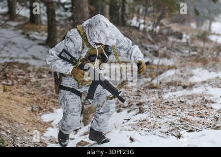 Soldat en camouflage d'hiver blanc escalade pente enneigée avec fusil pendant l'entraînement militaire Banque D'Images