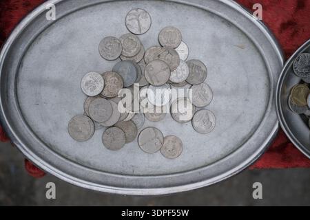 Vue aérienne de pièces de monnaie mélangées de couleur argent disposées lâchement sur un plateau métallique circulaire, aigles et chiffres en relief visibles, fond textile rouge Banque D'Images