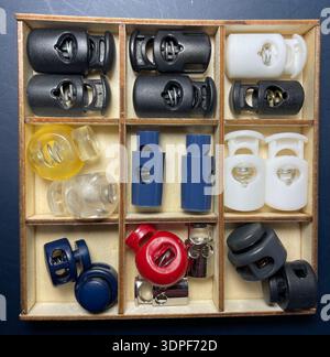 Plateau organisateur en bois vintage avec boutons-pression assortis, serrures à cordon, bascules à ressort, barils en plastique et composants métalliques dans les compartiments Banque D'Images