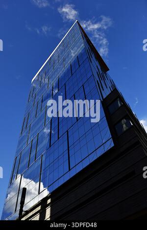 La vue en angle bas d'un bâtiment en verre bleu montre de fines fentes verticales de fenêtre et des reflets nuageux le long de la façade au coin, Denver, Colorado, États-Unis. Banque D'Images