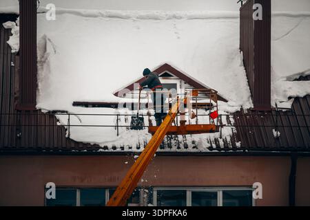 Un travailleur sur une plate-forme élévatrice nettoie la neige accumulée sur le toit d'un bâtiment après de fortes chutes de neige pour assurer la sécurité structurelle. Banque D'Images
