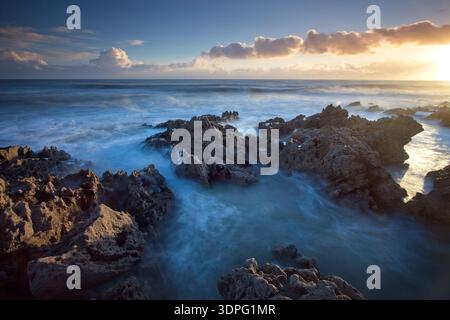 Coucher de soleil sur un rivage rocheux sur la péninsule de Gower, au pays de Galles, avec de longues vagues d'exposition, des nuages brillants et un large horizon atlantique au coucher du soleil. Banque D'Images