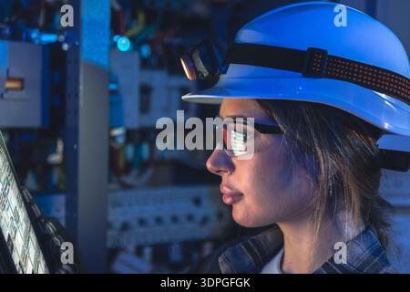 Une électricienne lit les données d'une tablette à côté d'un tableau de commutation. Maintenance intelligente. Banque D'Images