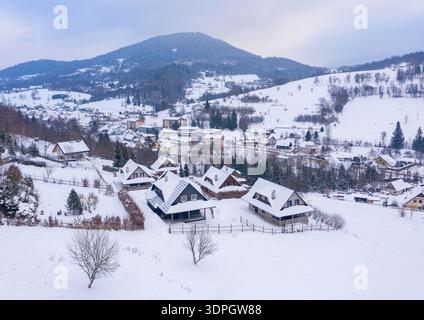 Vue aérienne des cabanes traditionnelles en bois dans le village enneigé de Terchova des montagnes Mala Fatra en Slovaquie avec paysage hivernal avec crique de neige blanche Banque D'Images
