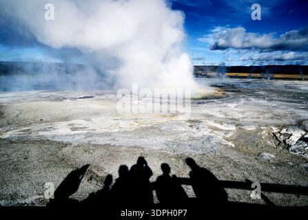 Les visiteurs regardent un geyser entrer en éruption dans le parc national de Yellowstone par une journée ensoleillée avec des nuages dans le ciel Banque D'Images