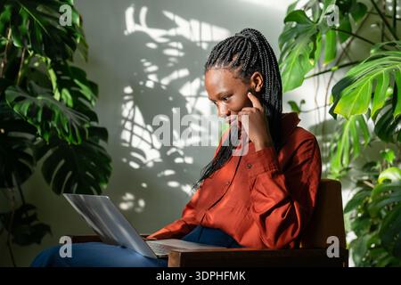 Surprise afro-américaine femme d'affaires freelance travaille sur ordinateur portable à la maison jardin vert tropical. Banque D'Images
