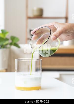 Verser à la main du matcha vert vif dans un verre de base de mangue et de lait, créant une boisson en couches Banque D'Images