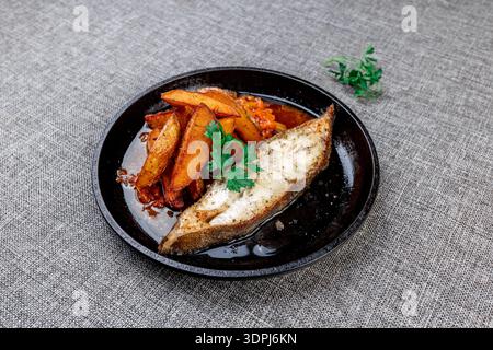 Un délicieux gros plan d'un steak de flétan parfaitement grillé servi avec des quartiers de pommes de terre rustiques et dorés et un mélange de légumes noir Banque D'Images