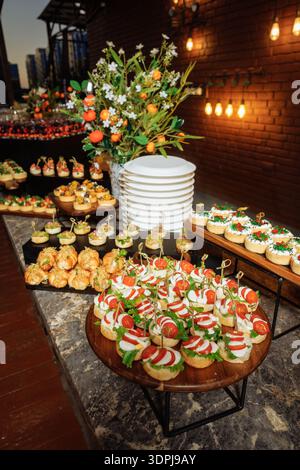 Buffet de luxe avec canapés assortis, bruschetta caprese sur brochettes, mini-hors-d'œuvre, fleur fraîche et orange sur plateau en bois Banque D'Images