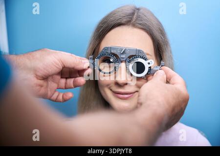 Jeune femme souriante avec monture d'essai pour la détermination du cristallin en clinique ophtalmologique Banque D'Images