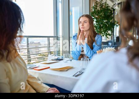 Jeune femme réfléchie assise avec ses amis dans le restaurant Banque D'Images