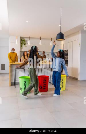 Famille avec deux filles dans des vêtements décontractés dansant près des bacs de recyclage dans la cuisine moderne Banque D'Images