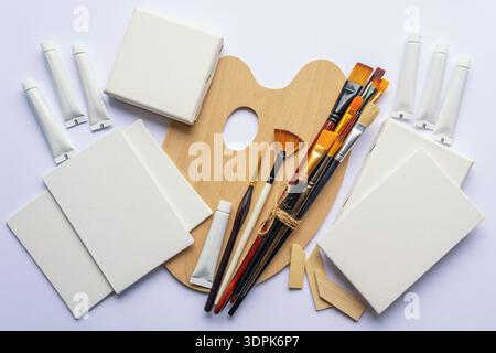 Outils artistiques. Palette, différents types de pinceaux, toile et tubes de peinture sur table blanche. Pose à plat, espace de copie Banque D'Images