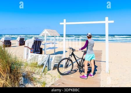 Jeune femme avec vélo debout sur le chemin de la belle plage de sable à Baabe sur l'île de Rugen, mer Baltique, Allemagne Banque D'Images