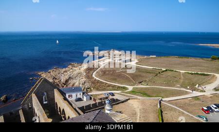 Une large vue côtière avec un phare surplombant les champs verdoyants et la mer, le tout sous un ciel bleu clair brillant. Banque D'Images