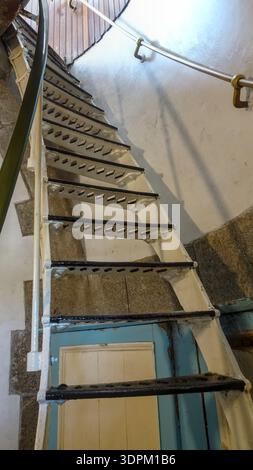 Un élégant escalier en colimaçon en fer avec une balustrade en métal serpente vers le haut dans un espace intérieur, mettant en valeur les détails architecturaux et l'artisanat. Banque D'Images