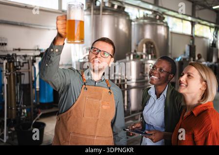 Brasseur inspectant la bière artisanale avec diverses femmes dans une brasserie moderne Banque D'Images