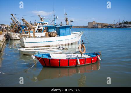 Trani, Italie - 16 octobre 2020 : plusieurs bateaux de pêche et petits bateaux sont amarrés dans le port avec un fort historique en pierre visible en arrière-plan sous un ciel bleu clair. Banque D'Images