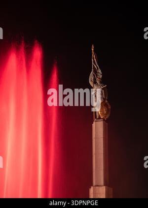 Mémorial soviétique de guerre Schwarzenbergplatz Vienne : statue de soldat avec drapeau et fusil, jets de fontaine rouge la nuit. Banque D'Images