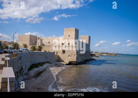 Trani, Italie - 16 octobre 2020 : le Castello Svevo en pierre historique avec des tours et des remparts est visible sur le front de mer, avec des drapeaux et des voitures garées à proximité sous un ciel partiellement nuageux. Banque D'Images