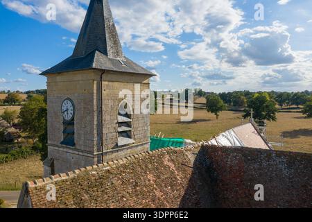 Eglise Saint Martin, France - 10 septembre 2020 : L'image montre la tour de pierre et la flèche en ardoise de l'église Eglise Saint Martin avec une horloge visible, un toit de tuiles rouges altérées, une bâche de protection blanche, un matériau de construction vert et un échafaudage, placés contre un paysage rural avec des arbres et des champs ouverts sous un ciel partiellement nuageux. Banque D'Images