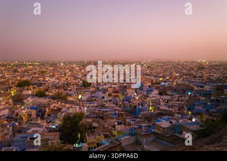 Jodhpur, Inde - 26 mars 2022 : une vue panoramique sur les bâtiments densément remplis de Jodhpur est vue au coucher du soleil, avec de nombreuses maisons peintes en bleu et des lumières de la ville visibles sous un ciel rosé. Banque D'Images