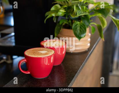 Deux mugs en céramique rouge assis sur le comptoir de café en pierre sombre exposant Latte art près de la machine à expresso Banque D'Images