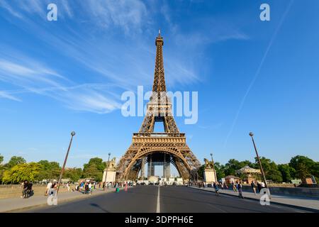 Paris, France - 10 mai 2022 : la Tour Eiffel est vue depuis le Pont d'Iena avec des gens marchant et faisant du vélo le long de la route et des trottoirs sous un ciel bleu clair. Banque D'Images