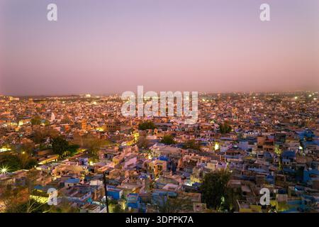 Jodhpur, Inde - 26 mars 2022 : une vue panoramique surélevée montre les bâtiments densément remplis de Jodhpur au crépuscule, avec de nombreuses maisons peintes en bleu et des lumières de la ville visibles sous un ciel rosé. Banque D'Images