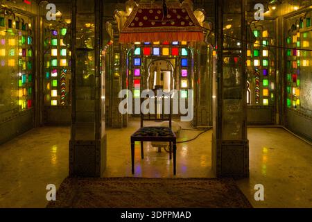 Udaipur, Inde - 24 mars 2022 : L'image montre une pièce richement décorée en miroir à l'intérieur du City Palace, avec des vitraux colorés, des panneaux muraux réfléchissants, une balançoire traditionnelle avec auvent et un sol recouvert de moquette. Banque D'Images