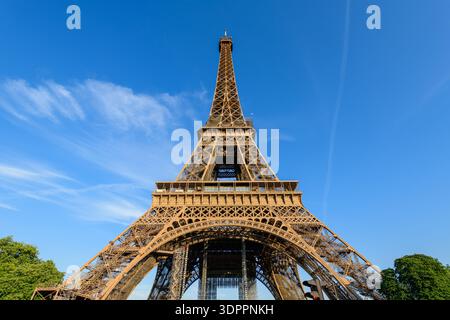 Paris, France - 10 mai 2022 : la Tour Eiffel est vue du niveau du sol avec sa structure en fer s'élevant contre un ciel bleu clair et un peu de verdure visible à la base. Banque D'Images