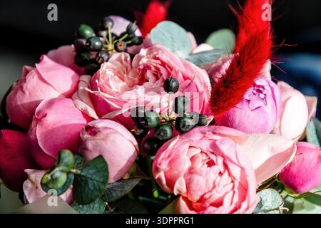 Gros plan d'un luxueux bouquet floral rose avec des roses de jardin, des baies foncées et un accent rouge vif. Idéal pour romance, mariages Banque D'Images