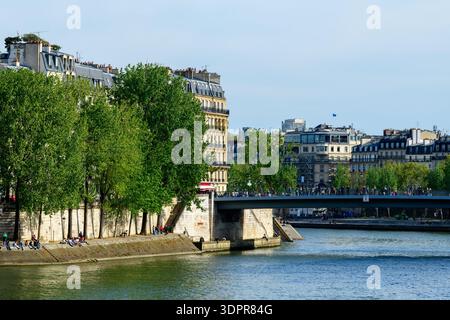Paris, France - 20 avril 2022 : le Pont Saint Louis traverse la Seine entre l'Ile de la Cité et l'Ile Saint-Louis, avec de nombreux piétons sur le pont, des arbres verdoyants le long de la rivière et des bâtiments historiques à plusieurs étages en arrière-plan. Banque D'Images