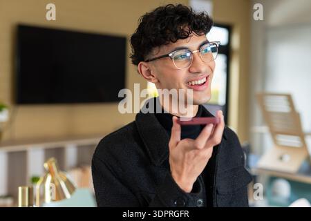 Homme d'affaires parlant dans le smartphone tout en souriant dans l'espace de travail de bureau avec moniteur, espace de copie Banque D'Images
