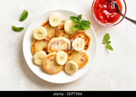 Délicieuses crêpes au fromage caillé avec tranches de banane servies avec sauce fraise. Beignets au Syrniki ou au fromage blanc pour un petit déjeuner ou un brunch sain. Lumière Banque D'Images