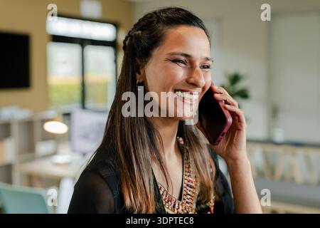 Femme indienne portant kurta tenant smartphone à l'oreille tout en se tenant debout par bureau dans le bureau, espace de copie Banque D'Images