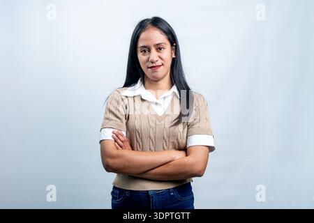 Une jeune femme asiatique dans un gilet beige et chemise blanche debout avec les bras pliés, regardant l'appareil photo avec une expression confiante sur un fond blanc Banque D'Images