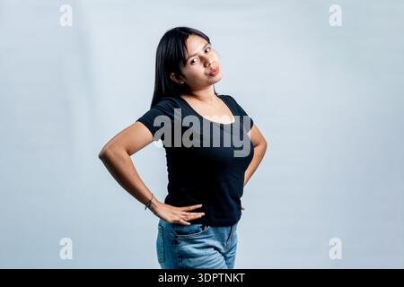 Une jeune femme asiatique confiante dans un t-shirt noir posant sur un fond blanc de studio. Banque D'Images