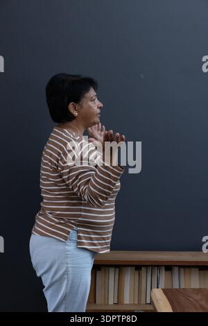 Femme levant les mains au niveau de la poitrine contre le mur gris avec étagère en bois et plateau de table Banque D'Images