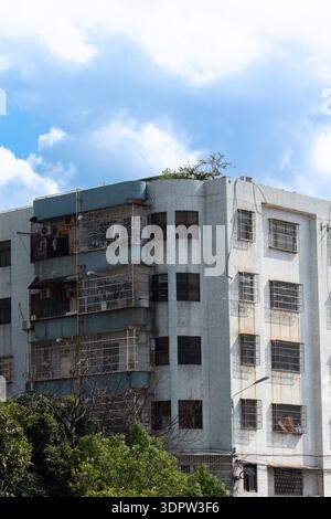 Immeuble d'appartements à plusieurs étages altéré avec balcons et verdure sous ciel nuageux dans la zone urbaine Banque D'Images