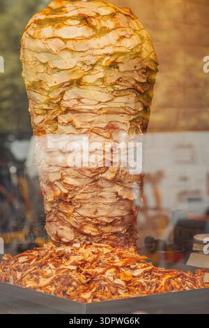 Shawarma de poulet grillé empilé sur une rôtisserie verticale, viande de shawarma de poulet tranchée recueillie dans un plateau, étal de nourriture de rue. Concept de poulet Banque D'Images