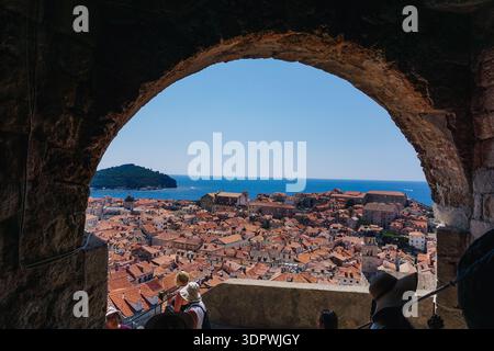 Vue de l'arc en pierre vieillie encadrant les toits en terre cuite vibrante en cascade vers la mer Adriatique Azur contre un ciel clair, Dubrovnik, Dubrovnik-Ner Banque D'Images