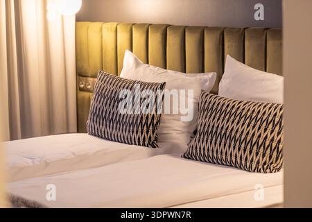 L'intérieur moderne et confortable de la chambre d'hôtel dispose d'un lit double soigneusement fait avec des draps blancs et des oreillers décoratifs à motifs. Éclairage doux et chaud et rembourrage Banque D'Images