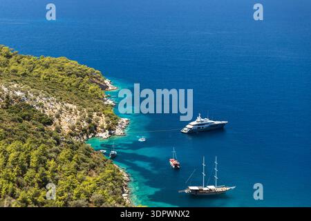 Vue aérienne d'une baie tranquille où plusieurs bateaux et yachts reposent près d'une côte rocheuse et parsemée de pins. Kalkan, Turquie. Contraste eau turquoise transparent Banque D'Images