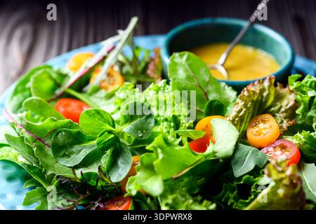 Salades vertes mélangées avec tomates cerises et vinaigrette sur table en bois, mélange de laitue fraîche. Style alimentaire naturel Banque D'Images