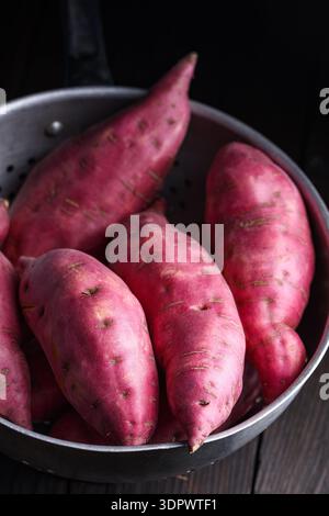 Patates douces fraîches dans un bol sur une surface sombre. Ingrédients végétaux naturels sains Banque D'Images