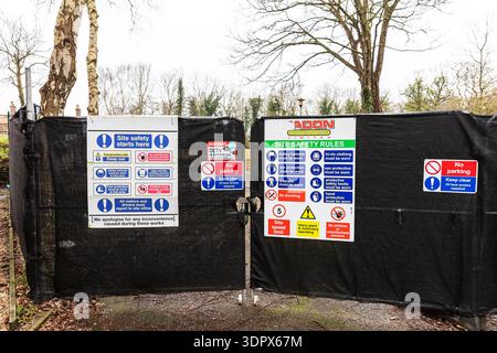 Entrée du chantier de construction affichant plusieurs panneaux de sécurité et avertissements, y compris les exigences en matière d'EPI, les règles du chantier, les avis de vidéosurveillance et l'interdiction de stationnement Banque D'Images
