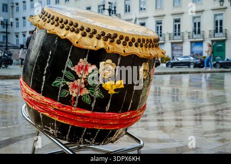 9 février 2024 - Lisbonne, Portugal : tambour chinois traditionnel en bois et en cuir altérés sur la place de la ville européenne, trottoir humide et reflets de bâtiment, pendant les célébrations du nouvel an lunaire. Diversité culturelle, multiculturalisme, intégration de la diaspora, Asie Banque D'Images