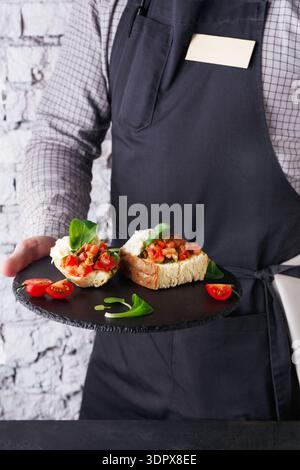 Le serveur sert une assiette de Bruschetta avec des garnitures fraîches dans un cadre de restaurant Banque D'Images