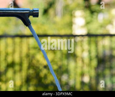 robinet de parc public avec l'eau sortant et le fond vert est flou Banque D'Images
